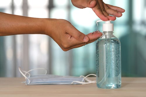 Free Crop unrecognizable person using antibacterial gel from transparent bottle on table near sterile mask during quarantine period Stock Photo