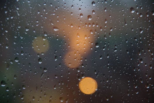 Close-up of raindrops on glass with city lights bokeh in the background, creating a moody atmosphere.