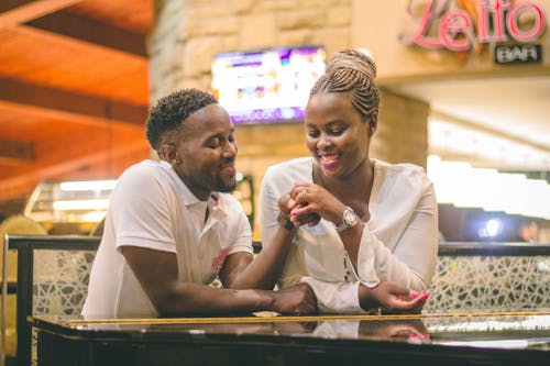 Cheerful African American couple with creative hairstyles sitting in cafe