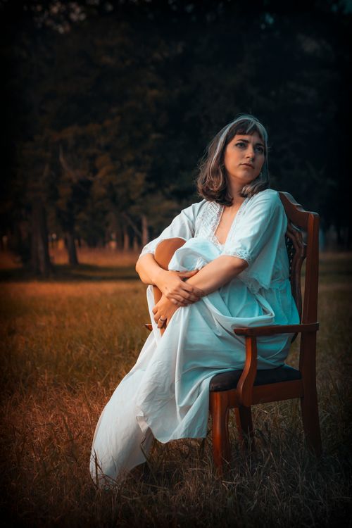 Free A serene portrait of a woman in a field chair, surrounded by nature during twilight. Stock Photo