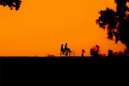 Two cyclists silhouetted against a vibrant sunset sky, enjoying a leisure ride.
