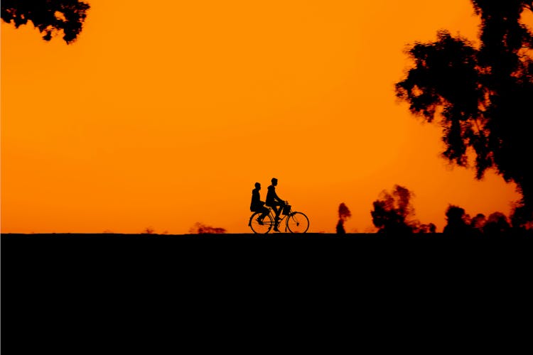 Unrecognizable People Riding Bicycle Against Sunset