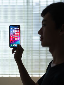 一名男子在室内背光处手持一部装有彩色应用程序的智能手机