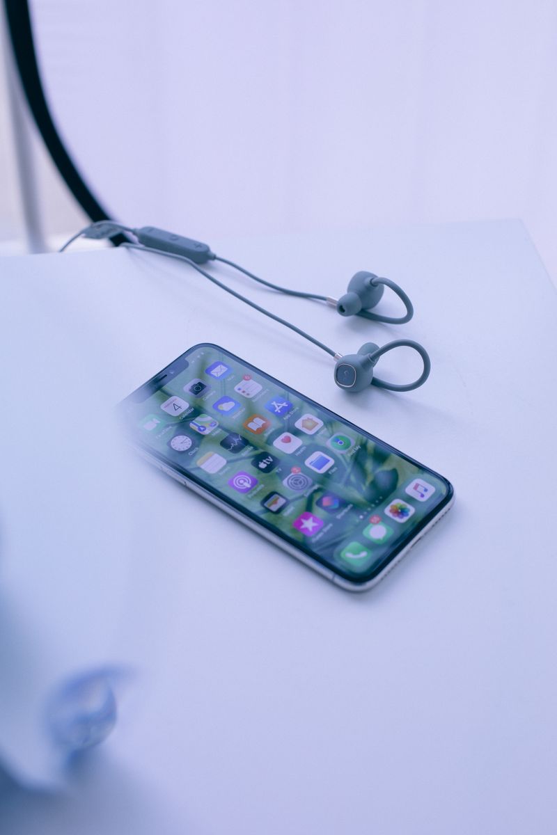 High angle contemporary switched on mobile phone placed on white desk near wired earphones