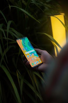 From behind crop unrecognizable person with contemporary mobile phone in hand near green houseplant