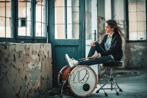 Free A young woman with drumsticks sits in an abandoned building, smiling and relaxed. Stock Photo
