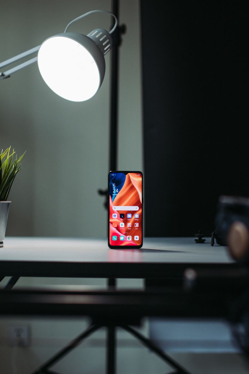 An indie developer reviewing app analytics on a laptop at a minimalist wooden desk with sticky notes and a smartphone nearby