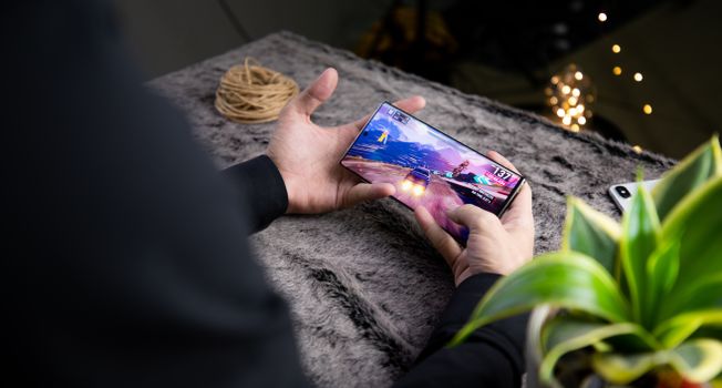 From above of crop anonymous person playing video game on modern cellphone with image of car on screen