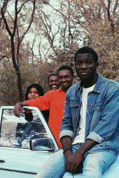 A joyful group of friends leaning on a blue car, surrounded by a forest, emphasizing friendship and adventure.