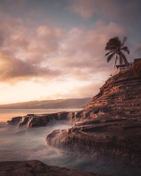 夏威夷岩石海岸线上，棕榈树与海浪映衬着宁静的日落景色