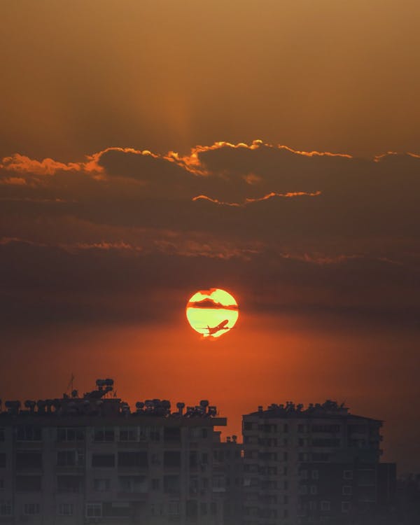 Breathtaking scenery of airplane flying over modern city buildings in picturesque cloudy sunset sky