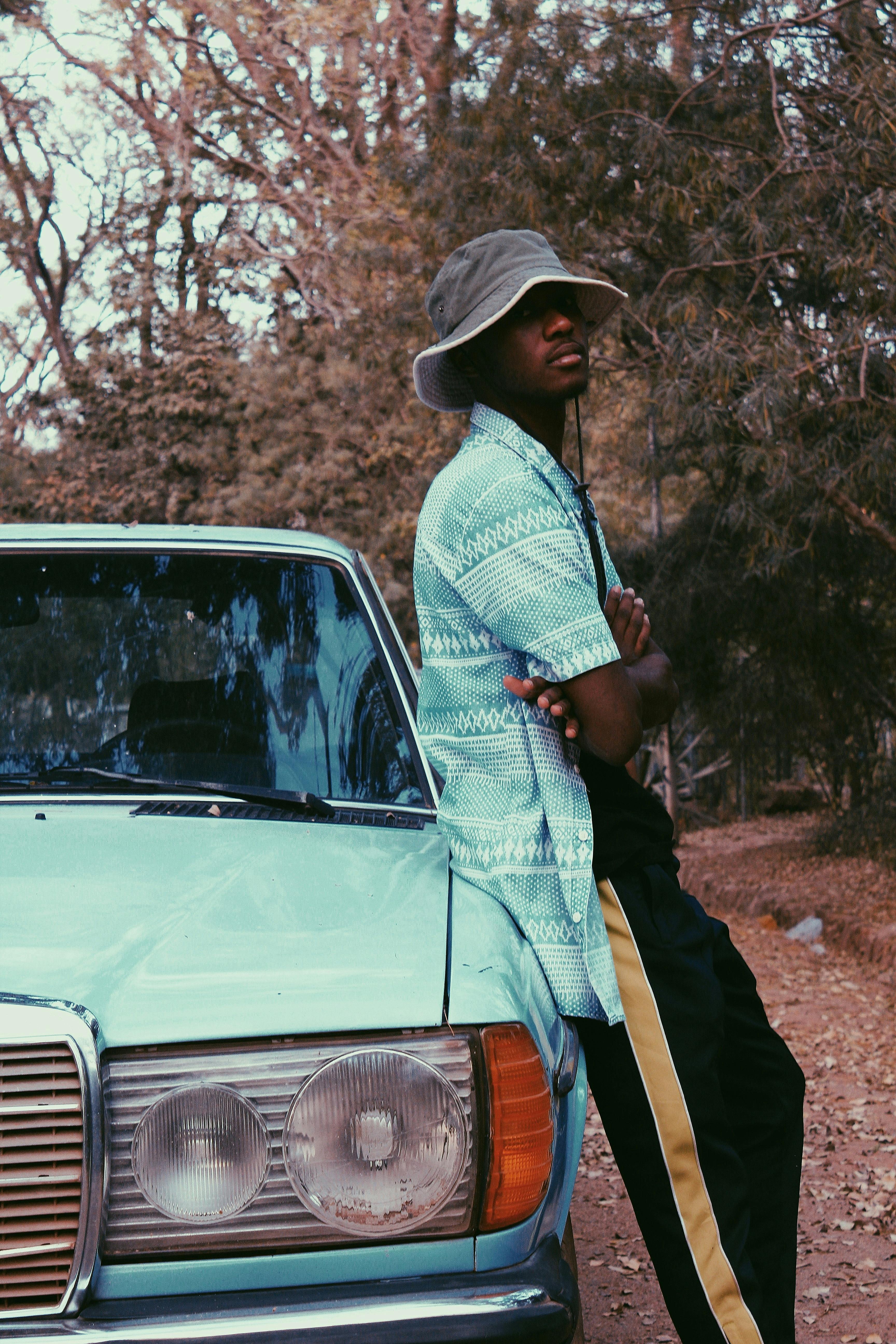man wearing gray bucket hat leaning on a blue vintage car