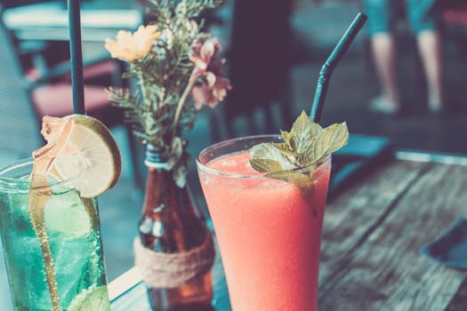 Glass of Fruit Juice Next to a Bottle With Flowers and Clear Glass Cup