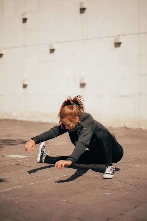 Young sportswoman stretching legs before workout on street