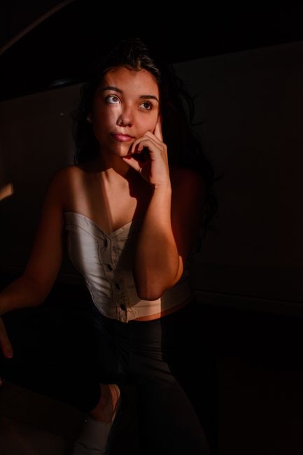 Pensive ethnic woman in trendy top leaning on hand while standing in sunbeam and looking calmly away