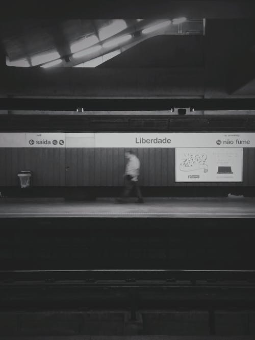 Grayscale Photo of Person Walking on a Train Station 