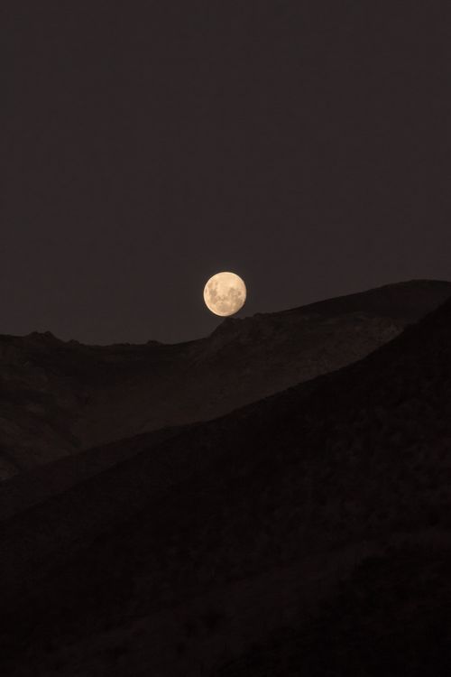 Free A captivating full moon rising over silhouetted mountains at night, creating a dramatic and serene scene. Stock Photo