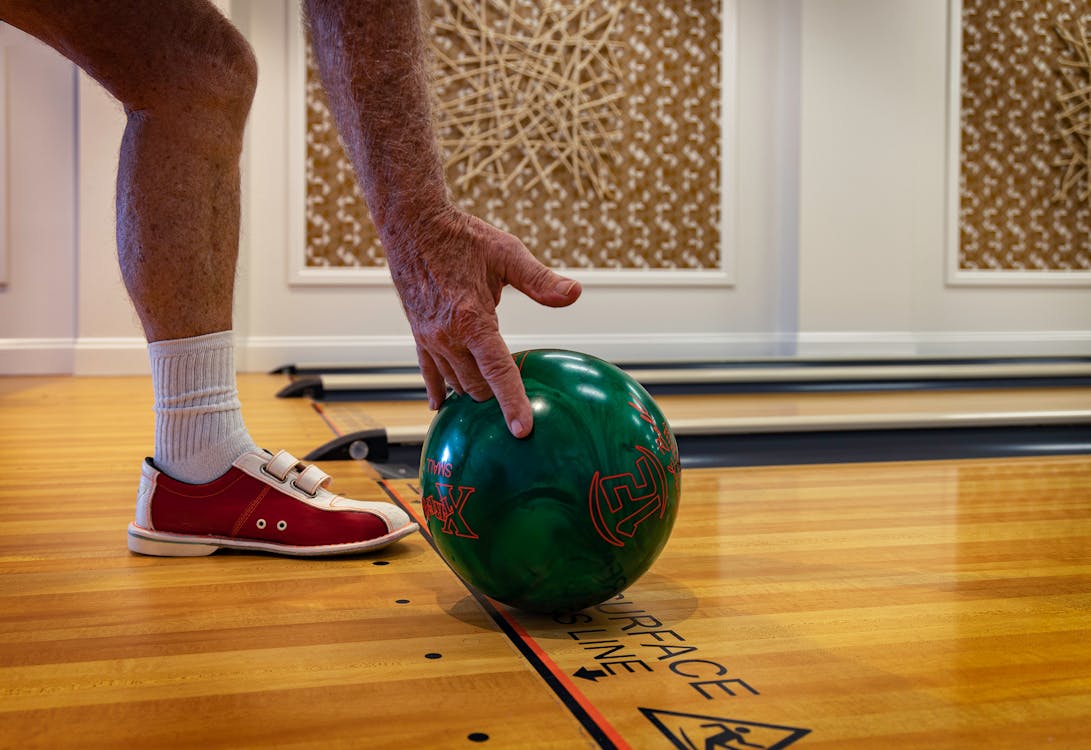 Free Crop anonymous sportsman in bowling shoes and socks rolling ball while playing bowling on wooden lane in modern bowling hall Stock Photo