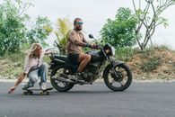 Man on motorcycle riding skater holding back of motorcycle