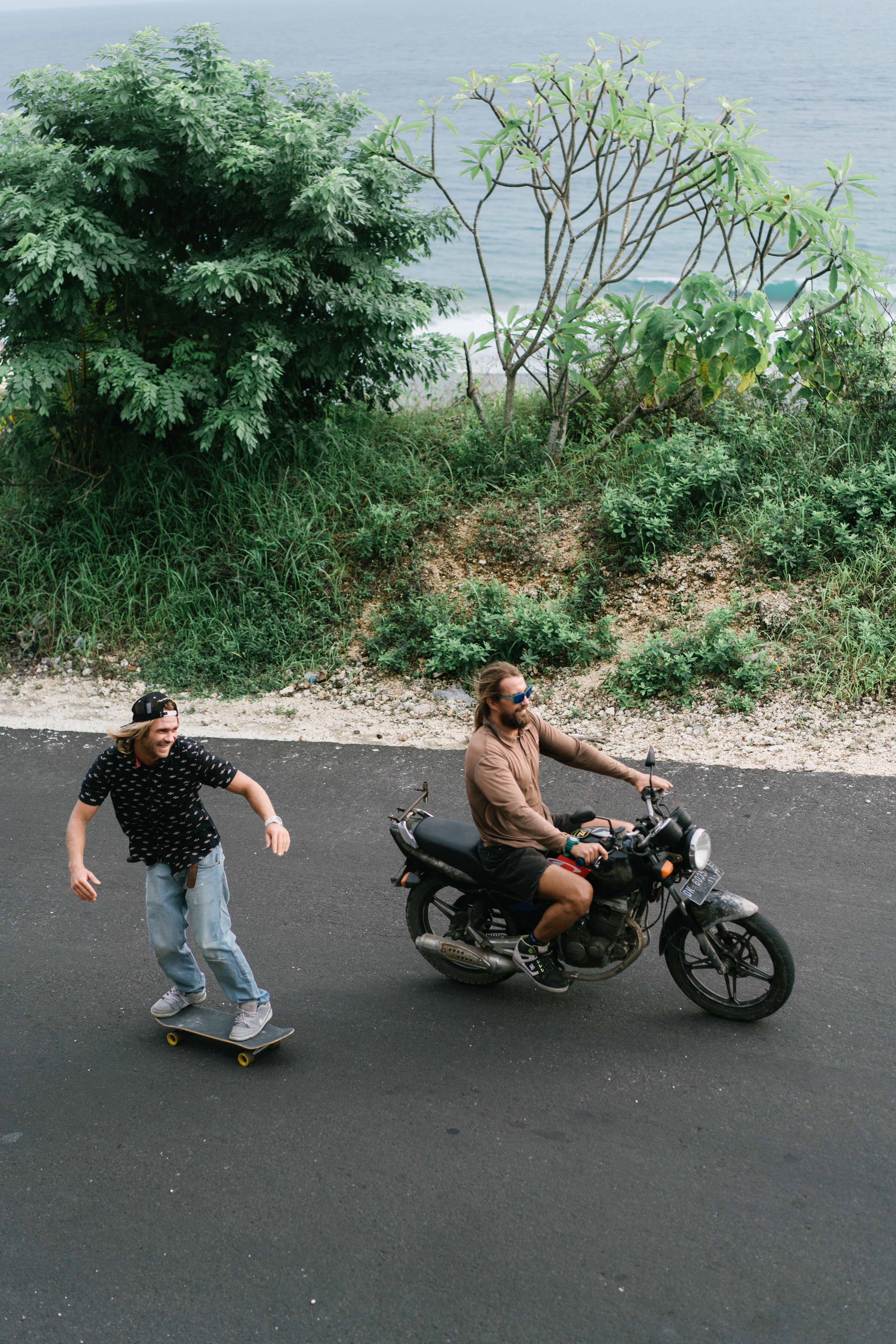 Content men riding bike and skateboard on seaside road · Free Stock Photo