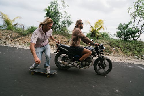 Man balancing on skateboard while being pulled by biker