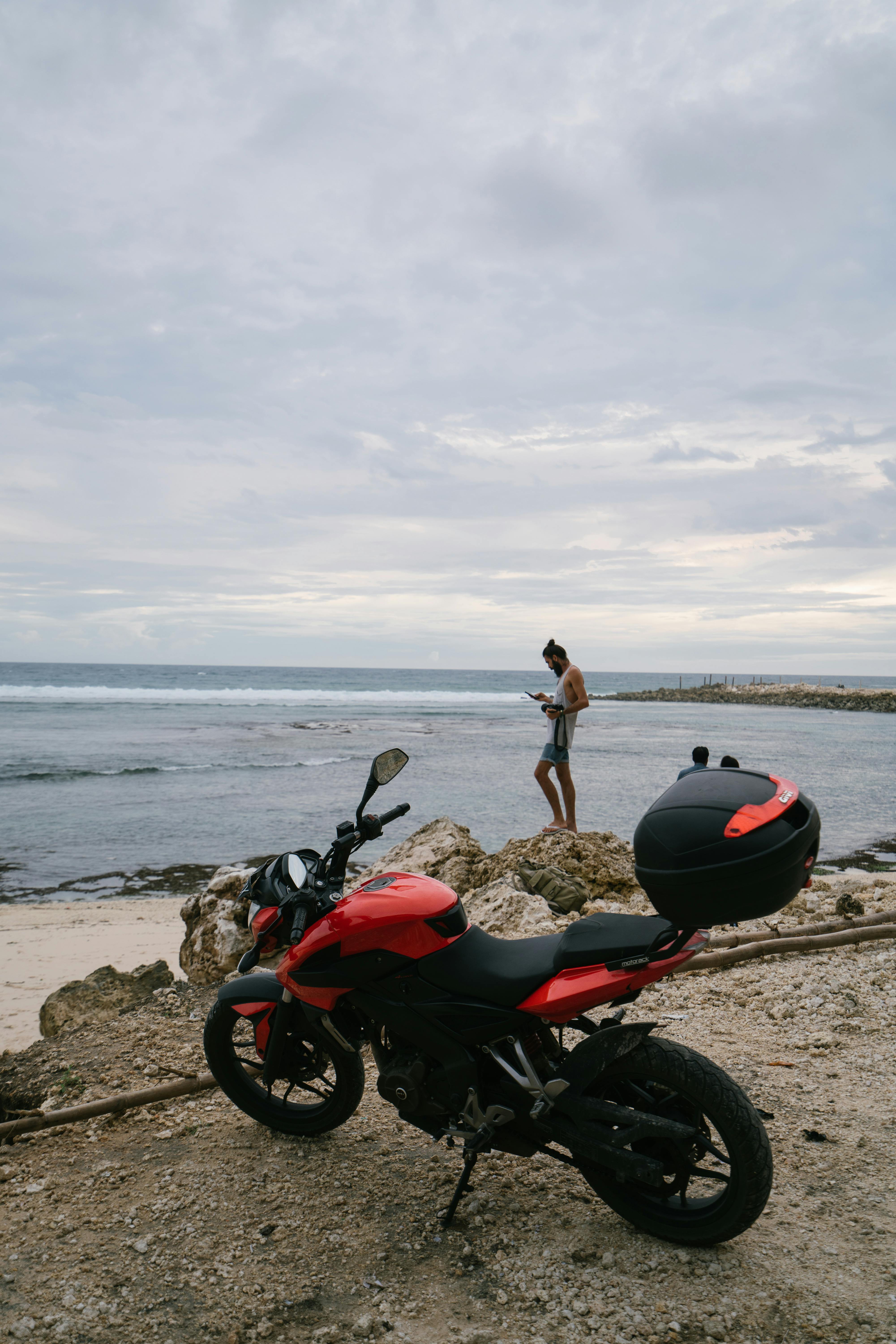 Unrecognizable man on seashore near motorcycle