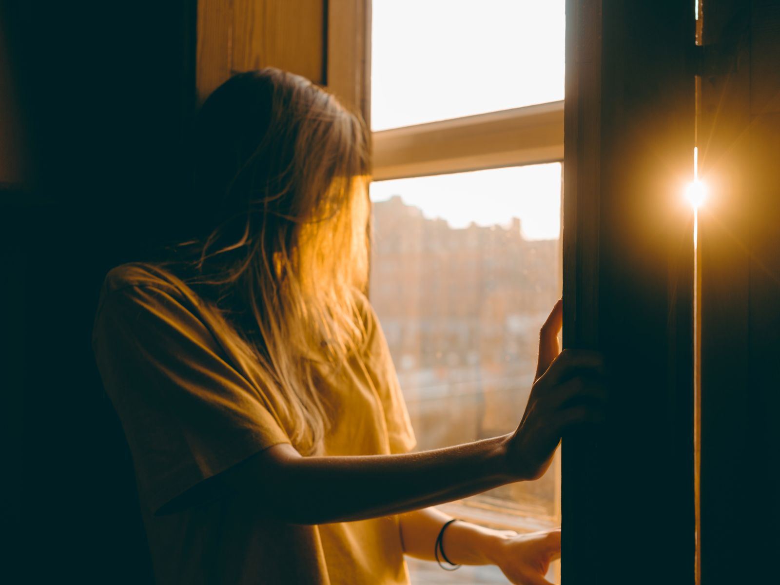 A woman stands at a window in Dublin during sunset, basking in warm sunlight.