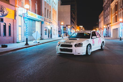 A sleek racing car parked on a vibrant city street at night, surrounded by colorful buildings.