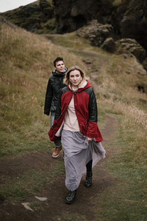 From above of young woman and man in warm outerwear walking on path among rocky mountain slope