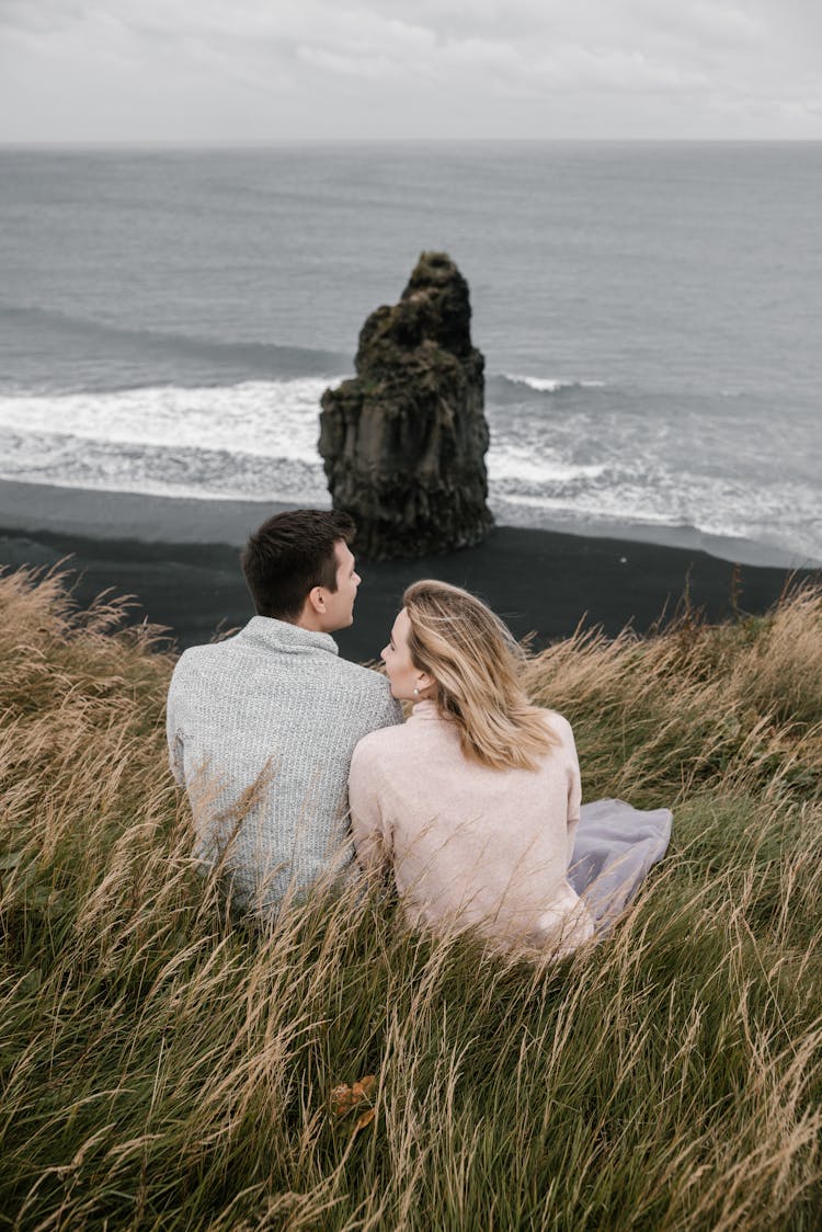 Couple Sitting In Grass On Black Sand Beach In Autumn