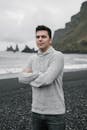 Young male standing arms crossed on beach on cloudy day