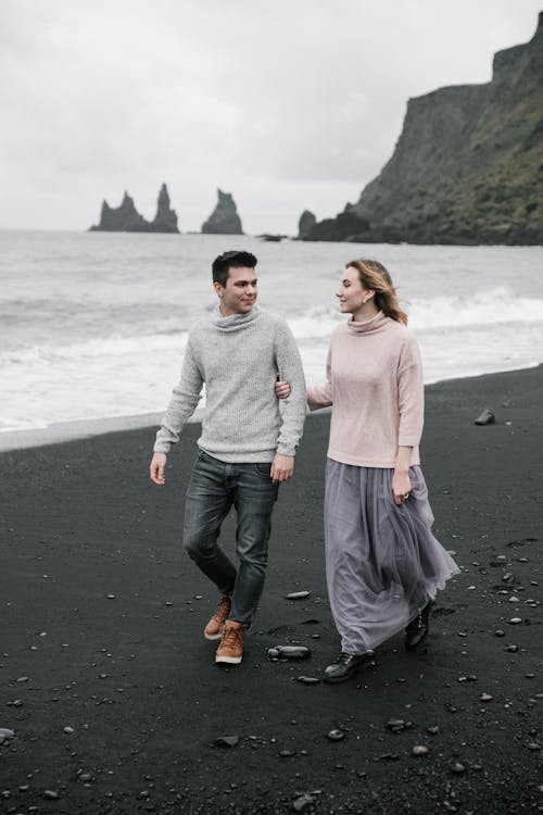 Couple walking along black sand beach with cliffs in distance