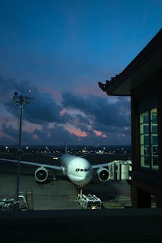 A serene view of an airliner parked at an airport gate during twilight with a dramatic cloudy sky.