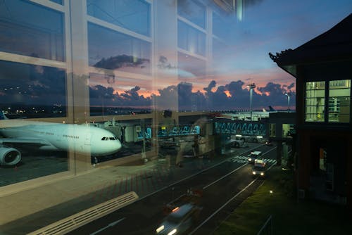 Through glass modern aircraft parked near airbridge in contemporary airport against picturesque dusk sky