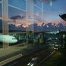 A commercial airplane parked at an airport gate, viewed through terminal windows reflecting a moody dusk sky.