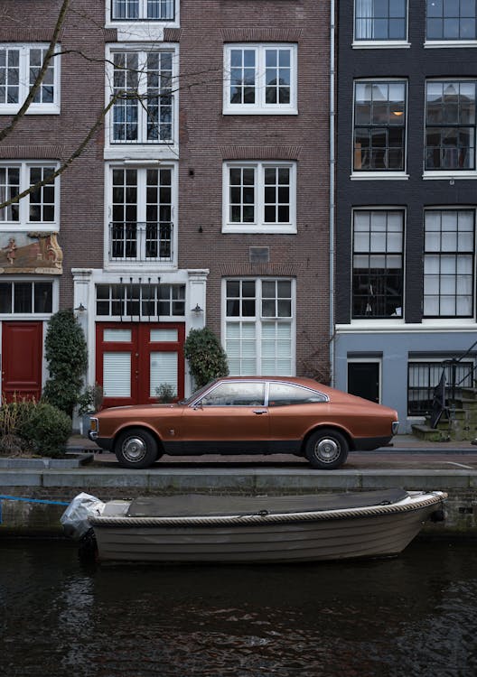 Free Retro car near canal with boat against narrow cozy houses Stock Photo