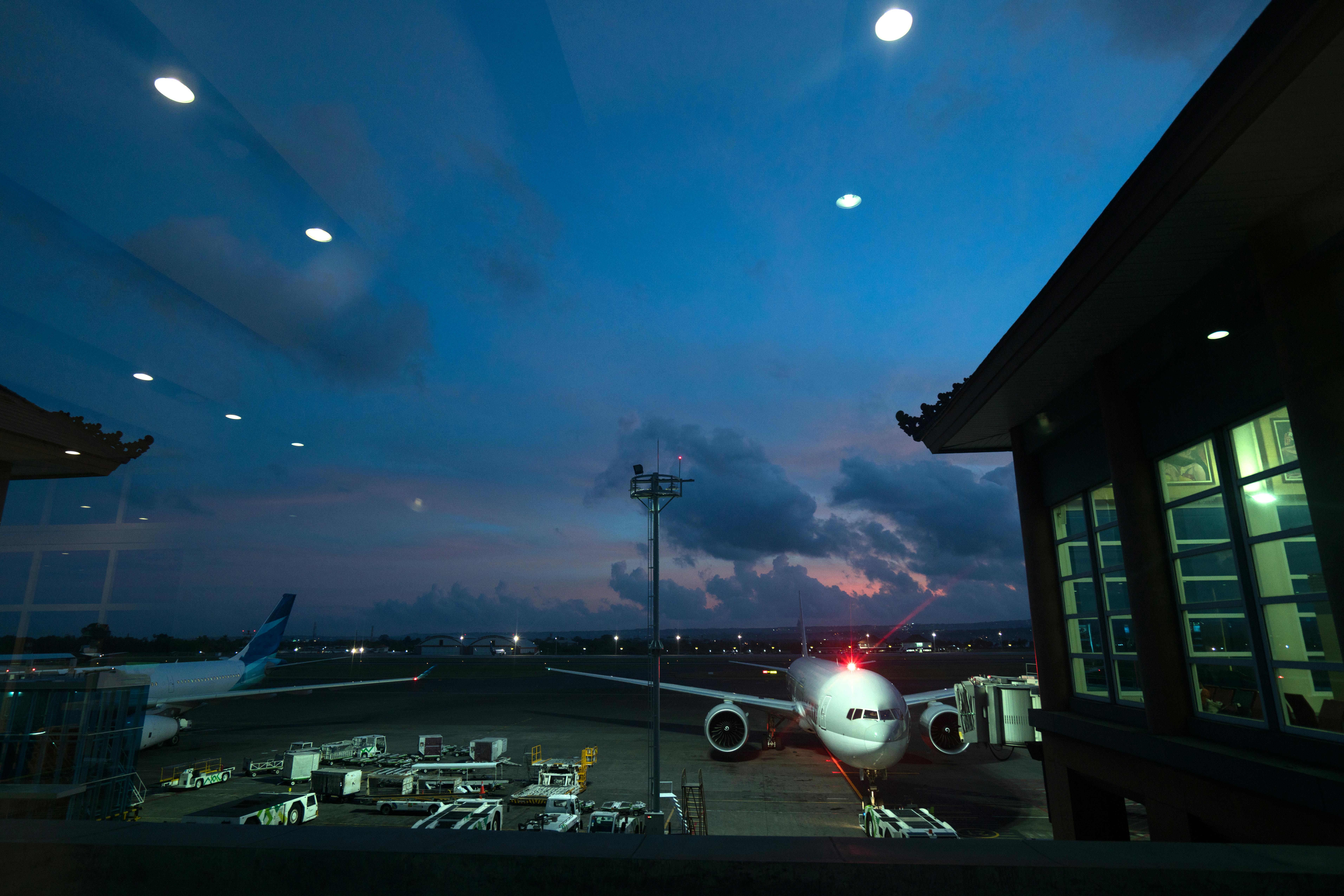 Contemporary airplanes with red beacon parked on airfield near airport service vehicles and terminal at night