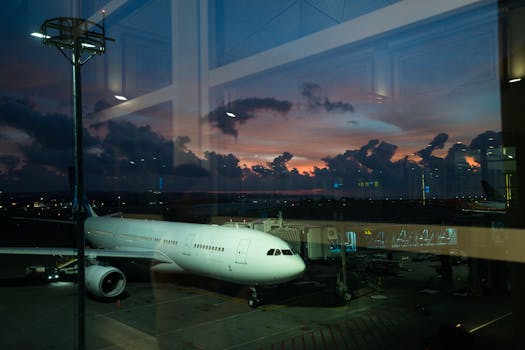 A modern airliner parked at an airport during sunset, reflecting in the terminal glass.