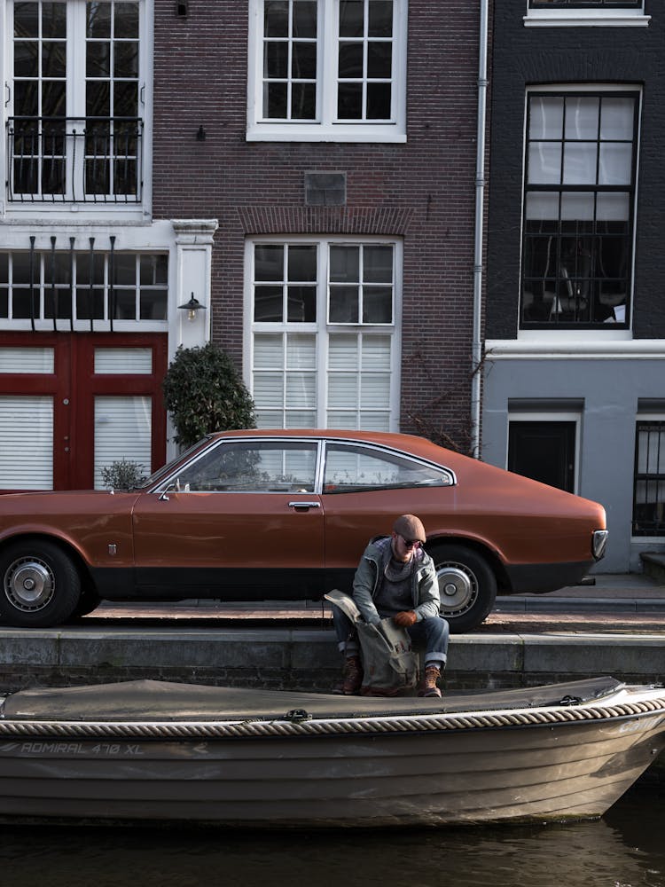 Man Sitting On Riverside Near Retro Car And Boat