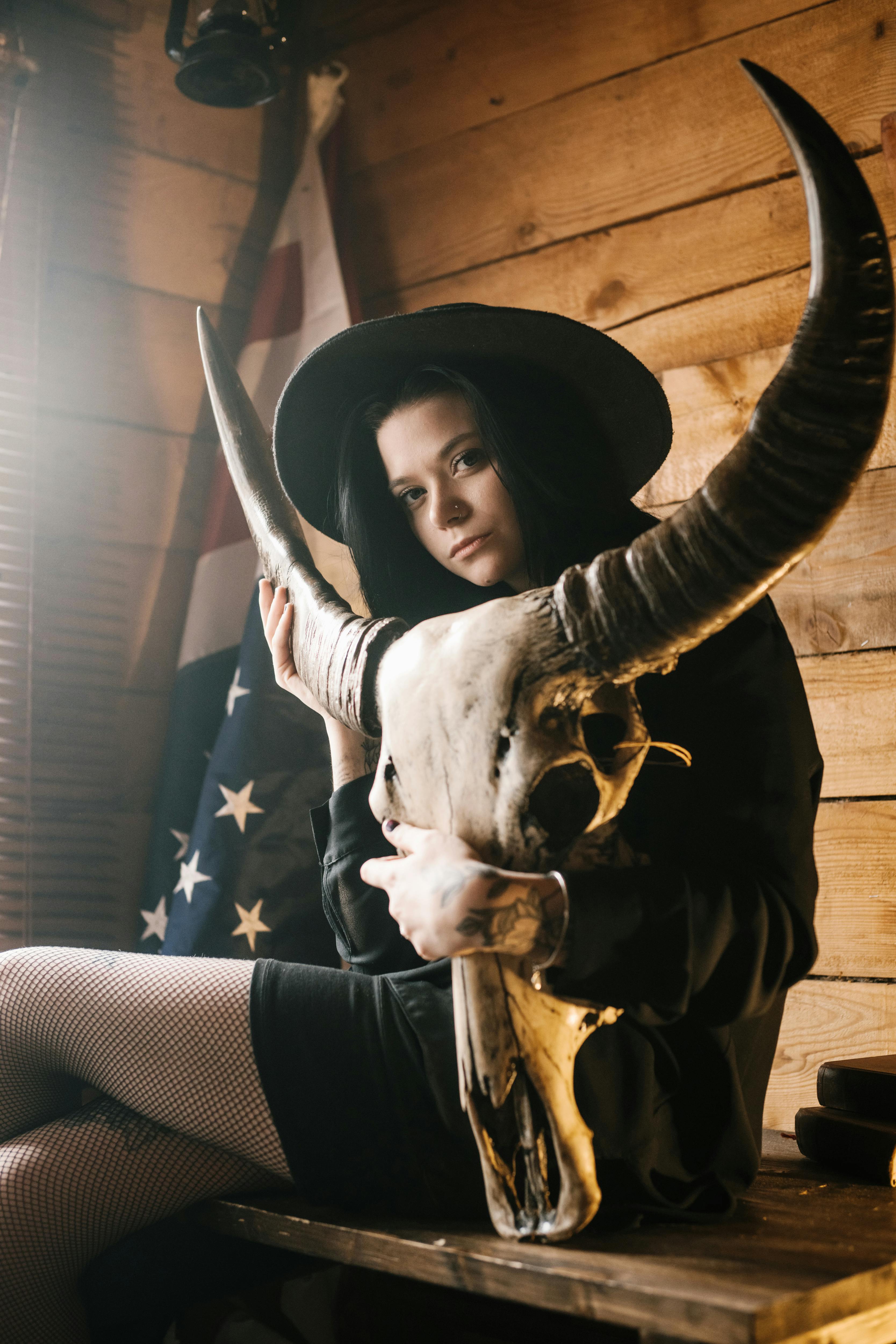 confident young woman in hat with long horned animal skull