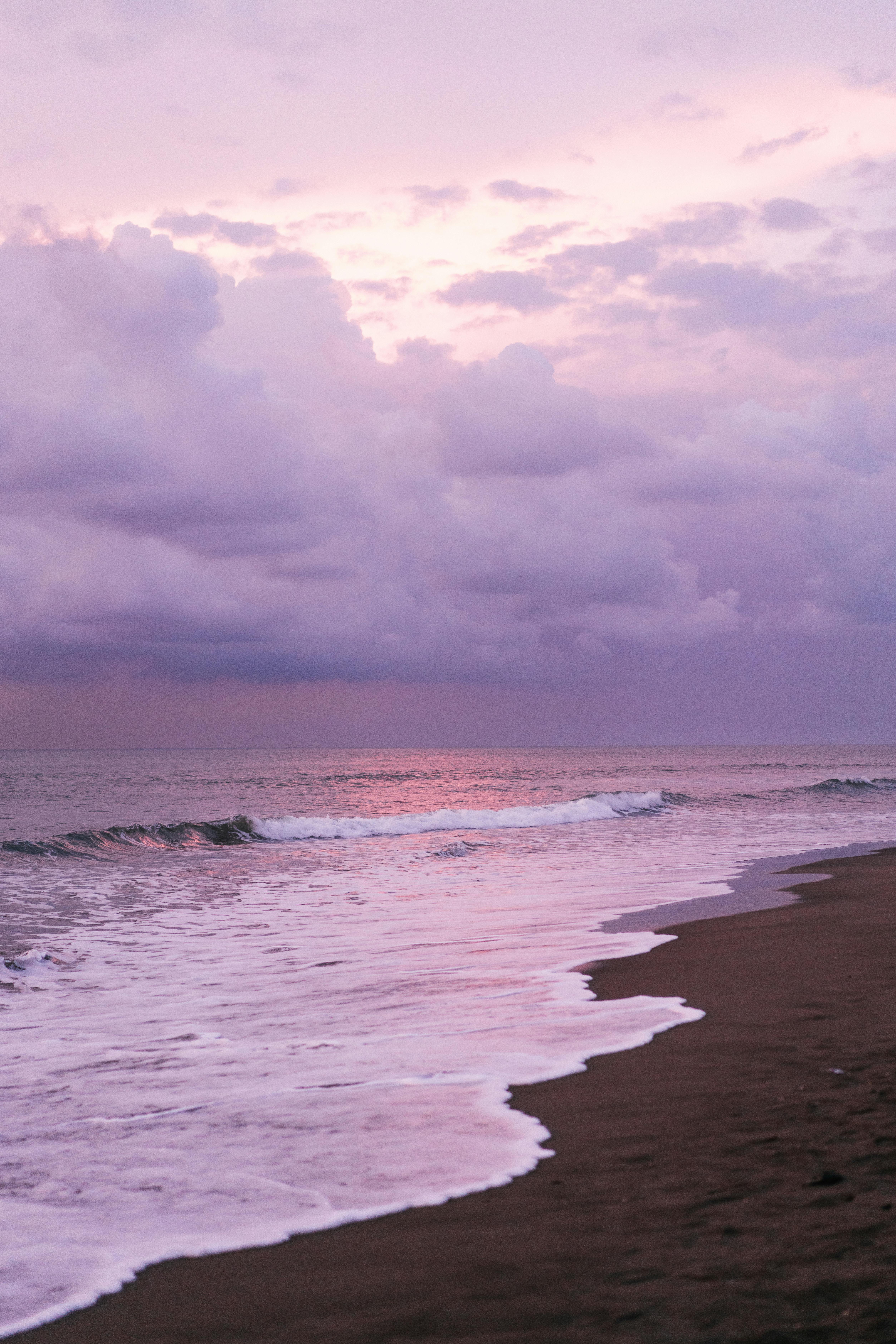 Amazing scenery of waving sea and sandy coast against picturesque cloudy purple sky at sunset time