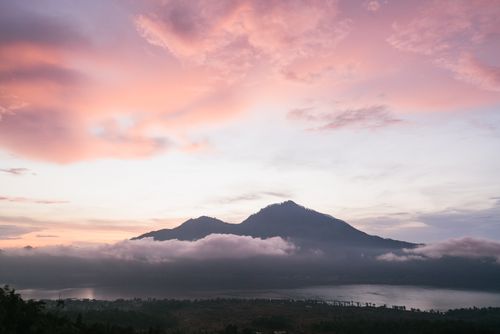 Free Breathtaking view of a mountain silhouetted against a pastel twilight sky with clouds and a lake. Stock Photo
