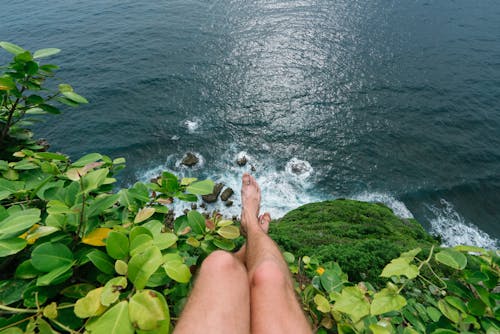 Faceless barefoot man sitting on high cliff