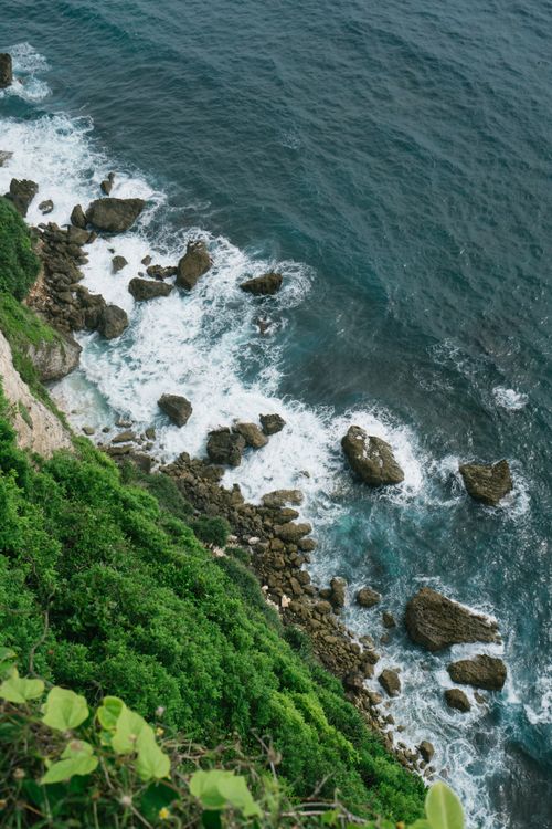 Free From above amazing scenery of rocky coastline with green moss and cliff over scenic seascape of waves hitting stones on the beach with turquoise sea water Stock Photo