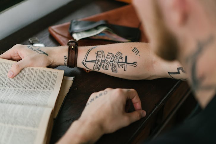 Crop man with tattoo on arm reading old book