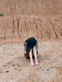 在大自然中休息时，一位女性将头放在膝盖上坐着，把脸藏了起来