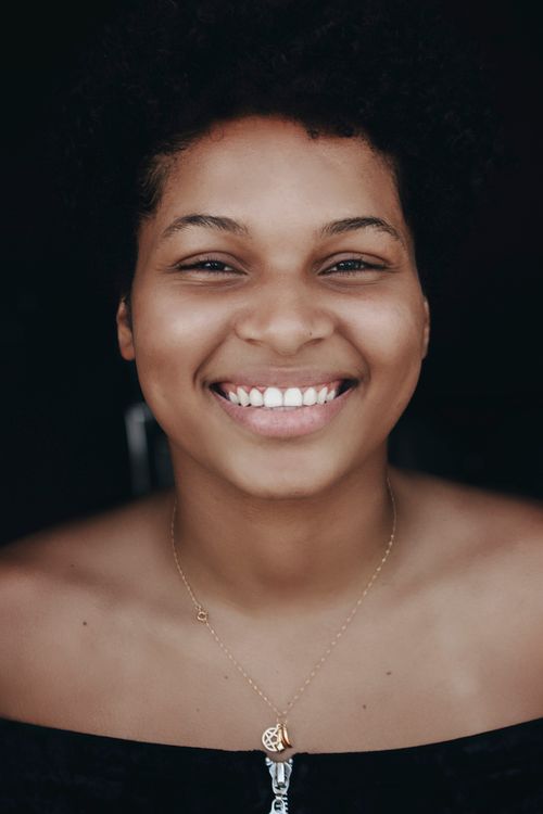 Free Bright portrait of a smiling woman, exuding warmth and positivity, set against a dark background. Stock Photo