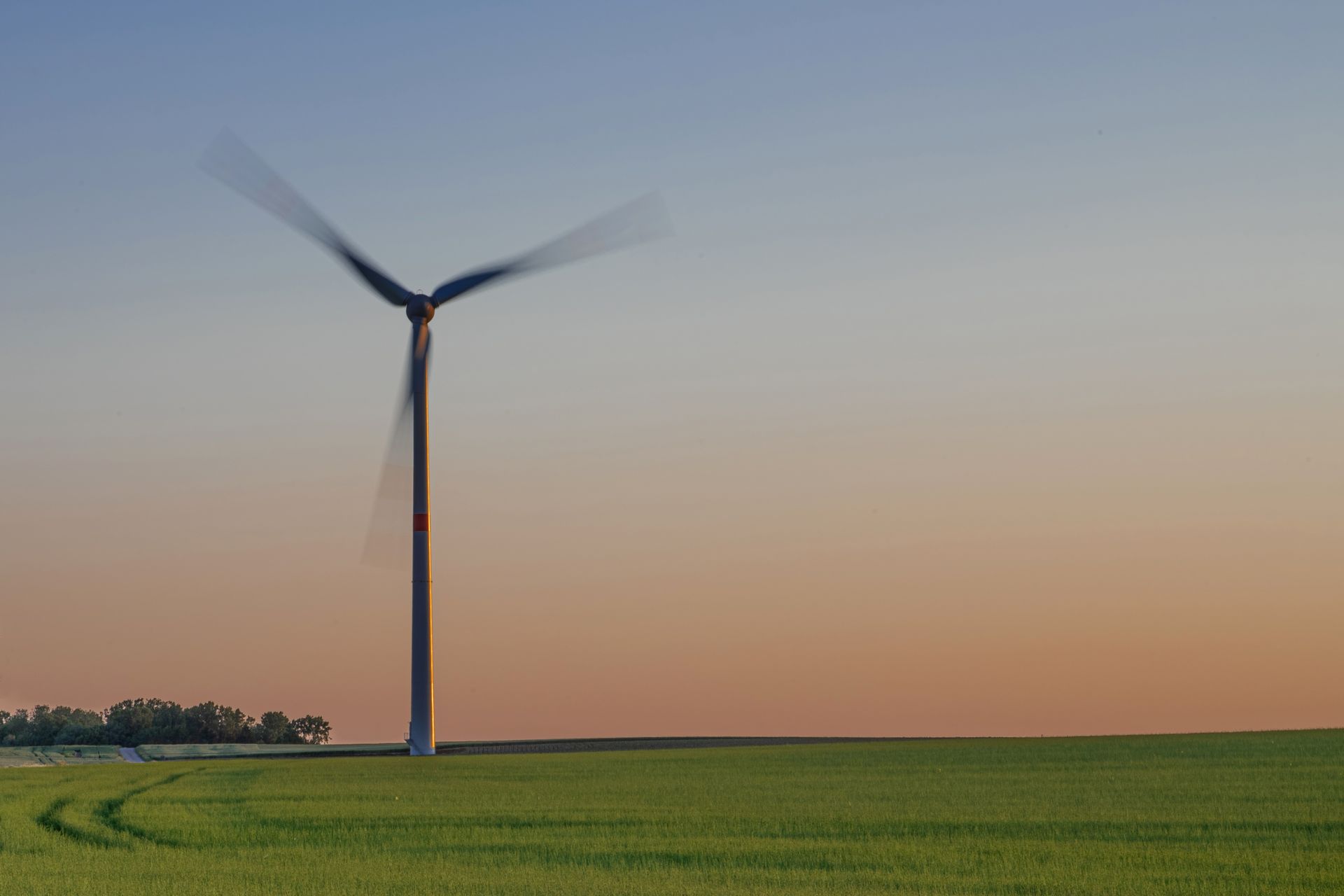 A wind turbine stands tall in a green field during sunset, symbolizing renewable energy in nature.