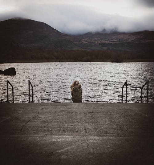 A Woman Wearing a Jacket Sitting by a Lake