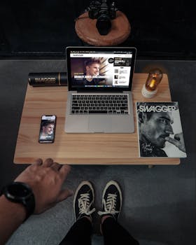 High-angle view of a stylish workspace featuring a laptop, magazine, and electronic devices.